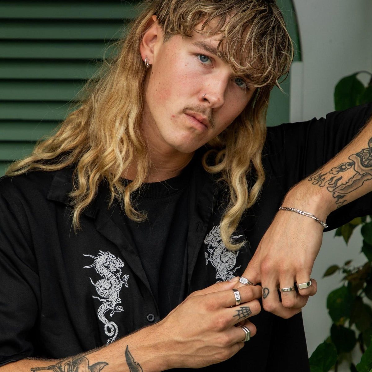 A cool, edgy shot of a male model with a mullet and tattoos, wearing the sterling silver Billie Jo Lumina hoop earrings and a collection of rings.