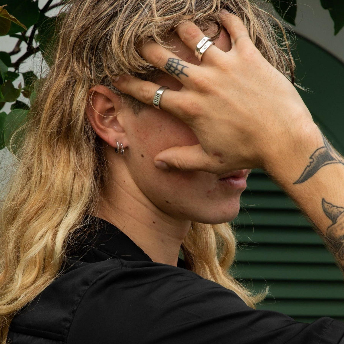 A male model with long blonde hair wears the sterling silver Billie Jo Lumina hoop earrings and matching silver rings, creating a stylish, layered look.