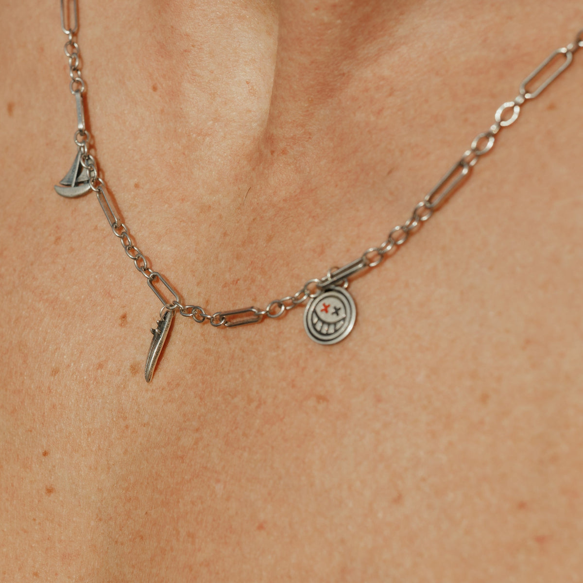 Close-up of the Billie Jo Freedom Necklace on skin, detailing the sterling silver paperclip chain and the smiley, boat, and feather pendants.