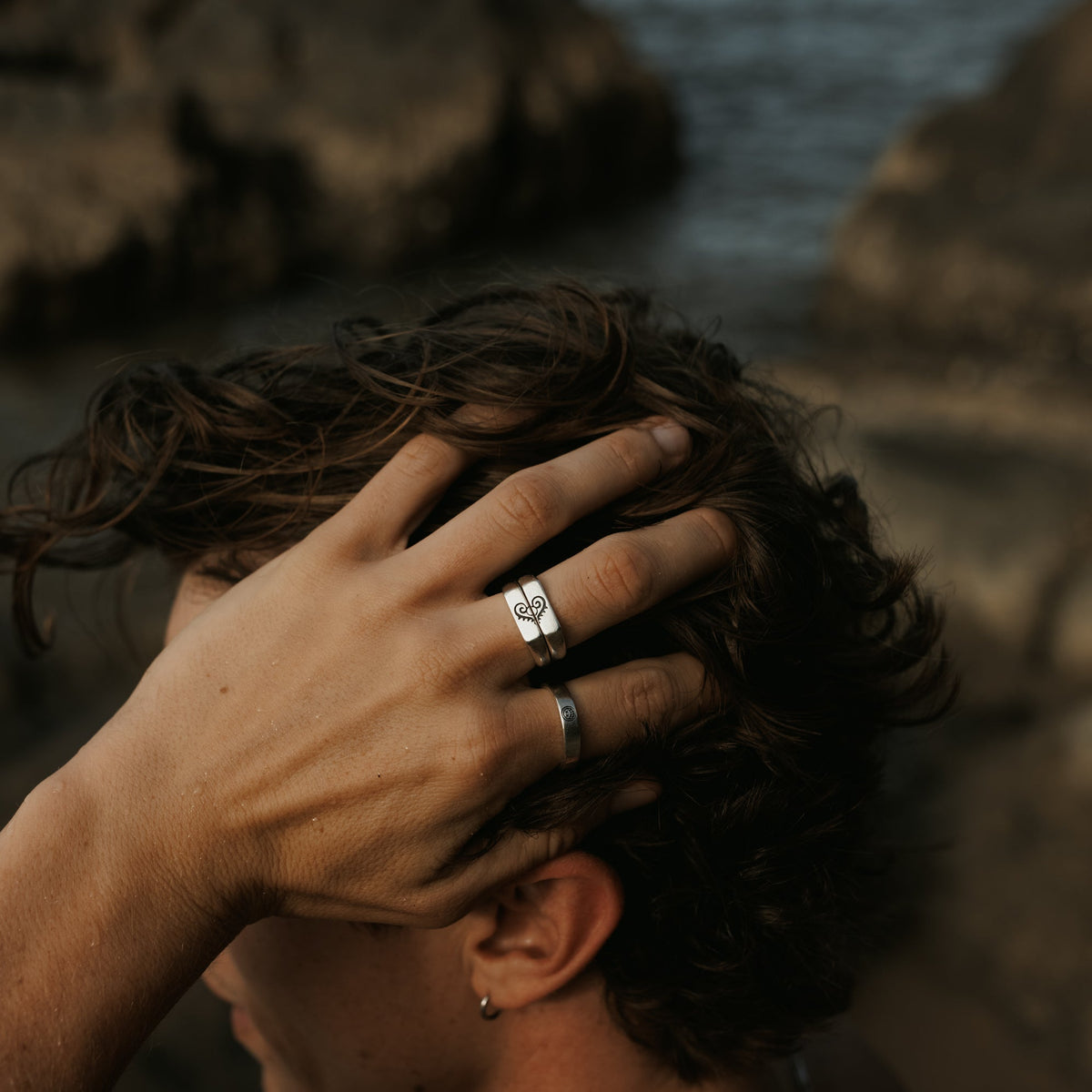 A man with his hand in his hair, wearing the Billie Jo Reflection Ring and another silver ring. This editorial shot captures a relaxed, masculine vibe.