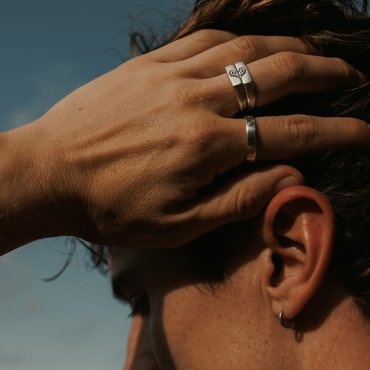 A man wearing the Billie Jo Connection Stackers rings, running his hand through his hair outdoors. Men's jewellery styling inspiration from Australia.