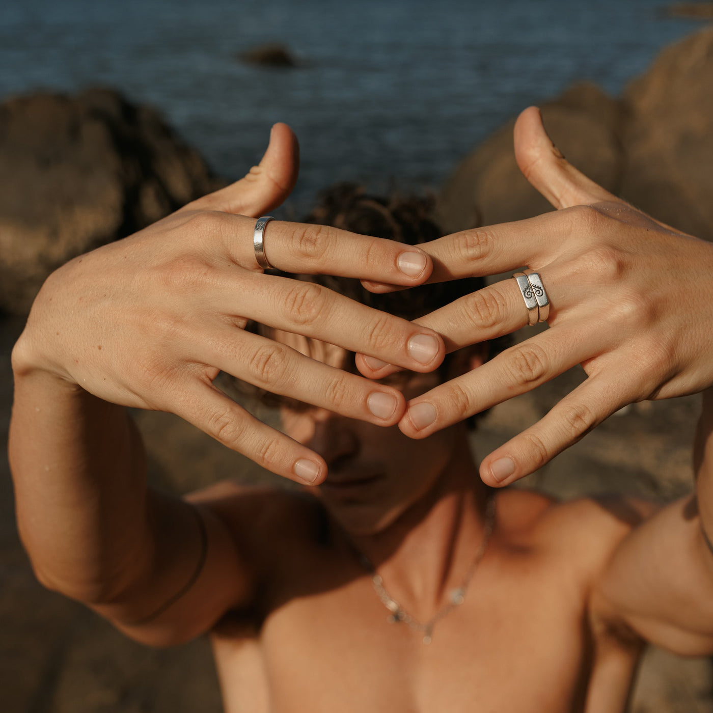 A man's hands held up to his face, showcasing the Billie Jo Reflection Ring on his left hand and another silver ring on his right, in a cool editorial shot.