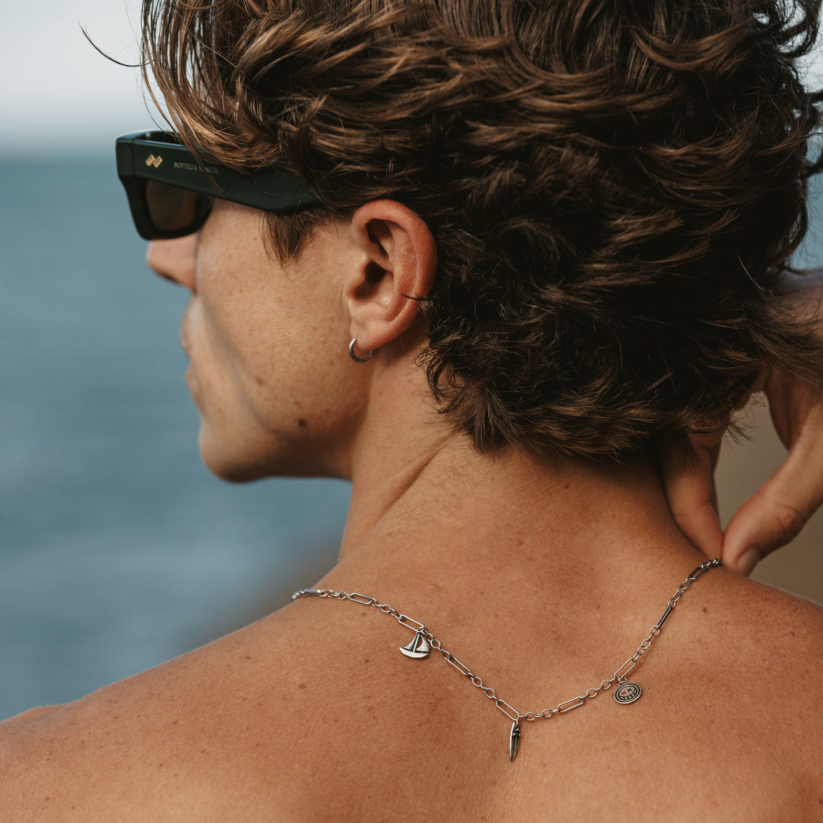 Back view of a man wearing the sterling silver Freedom Necklace by Billie Jo, showing the paperclip chain and pendants resting on his shoulders in the sun.