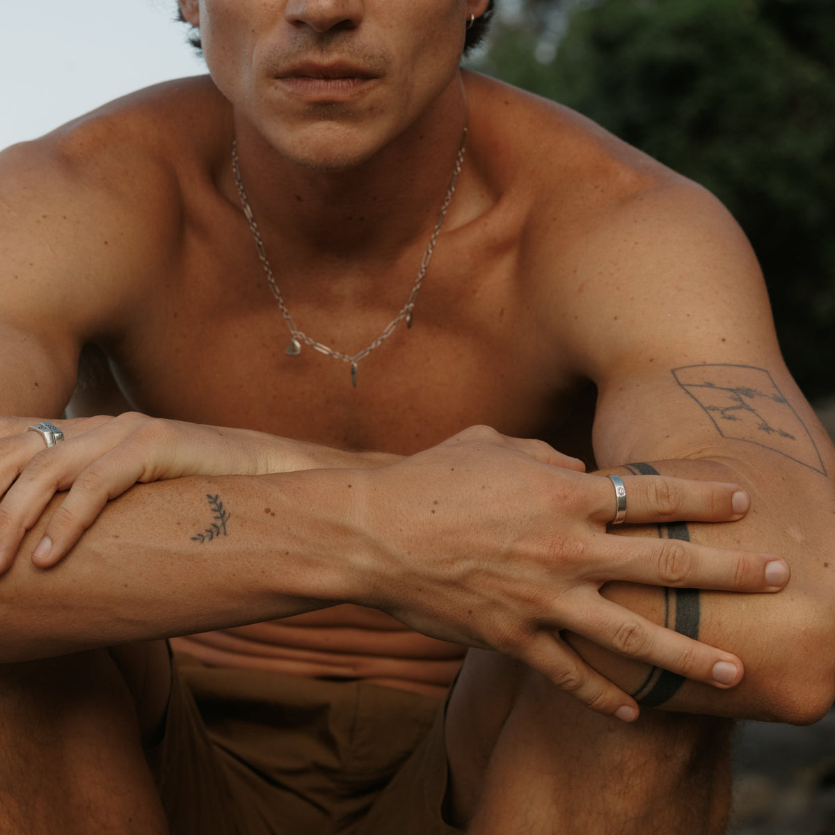 A man wearing the Billie Jo Reflection Ring on his right hand, part of a stylish, layered jewellery look with a silver necklace and other rings.