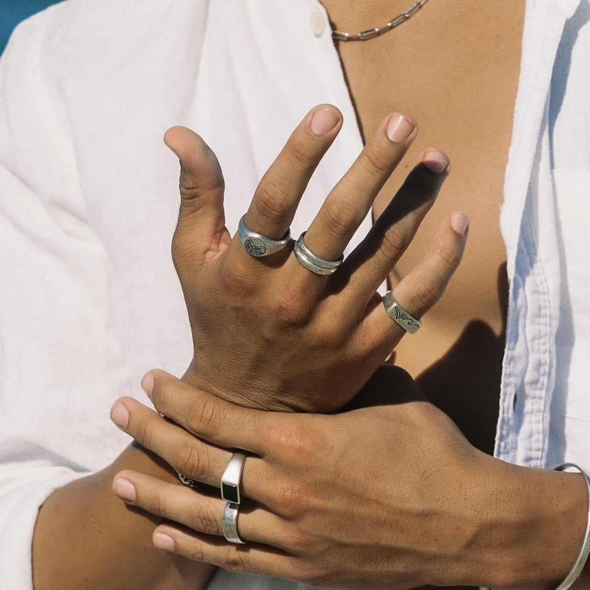 A close-up of a man's hands, showcasing a stack of silver rings including the Billie Jo Current Ring, against a white linen shirt.
