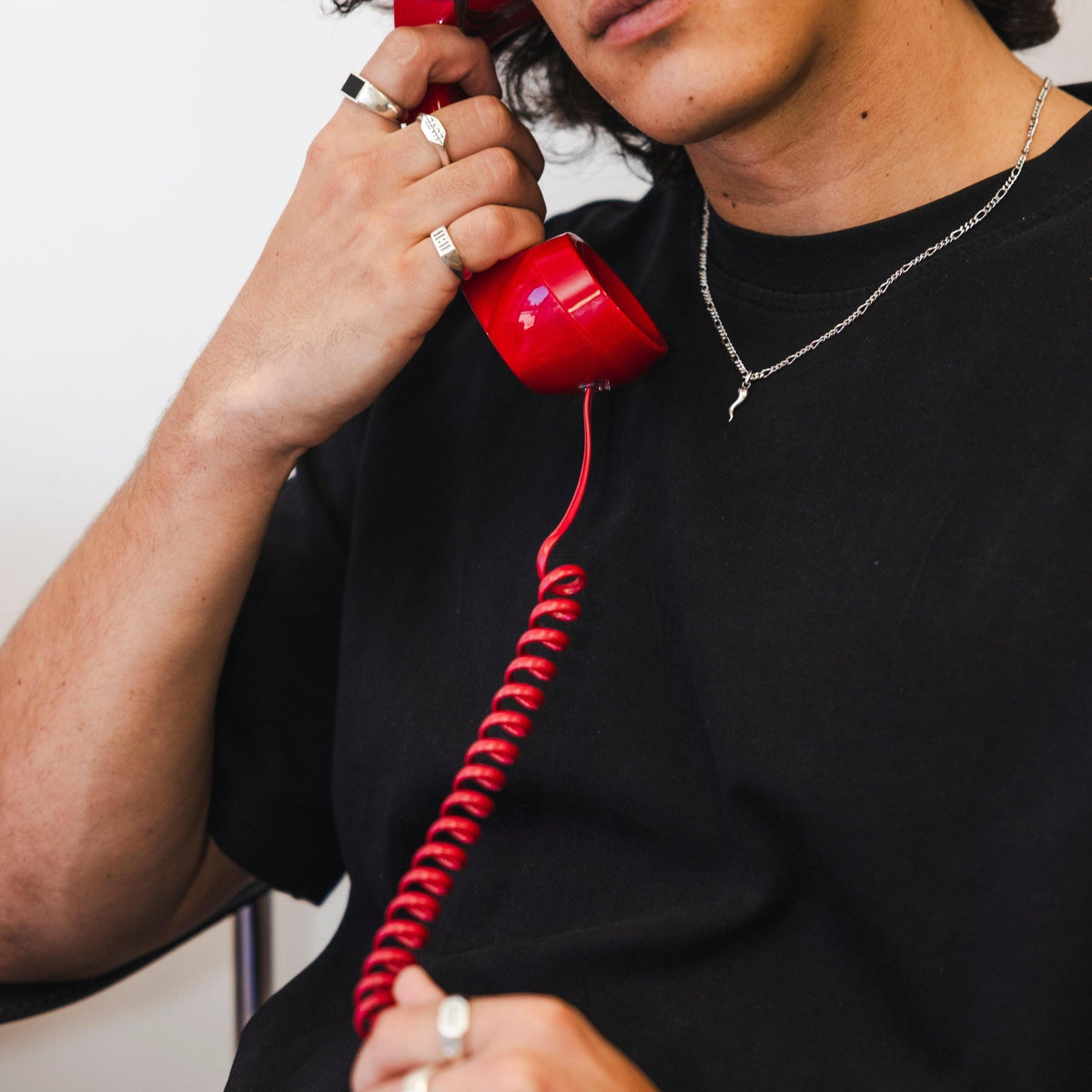 An editorial shot for Billie Jo featuring a model on a red telephone, wearing the silver Chilli Pendant with a black t-shirt and a collection of silver rings.