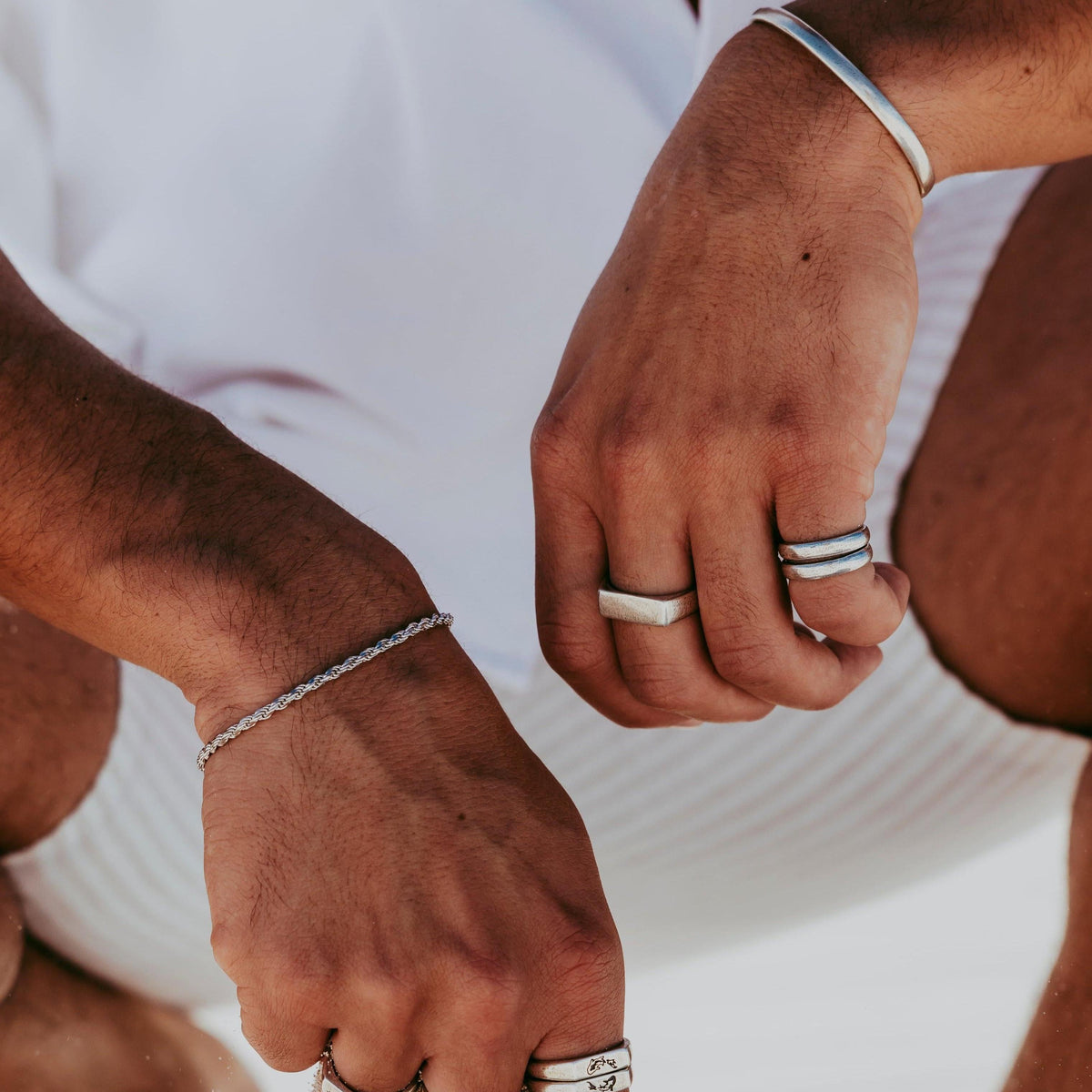 A close-up lifestyle shot of a man wearing a collection of Billie Jo sterling silver rings and bracelets, highlighting the texture and design of the Stacker Rings.