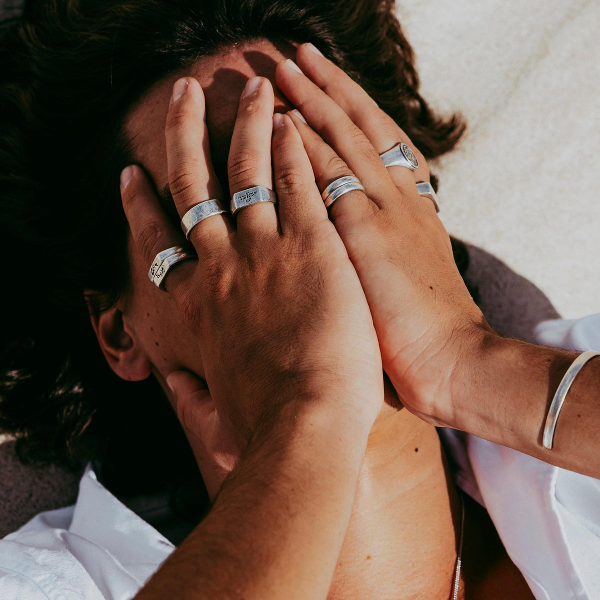 A man's hands adorned with multiple sterling silver Billie Jo Stacker Rings, captured in a sun-drenched editorial shot that evokes a sense of effortless style.