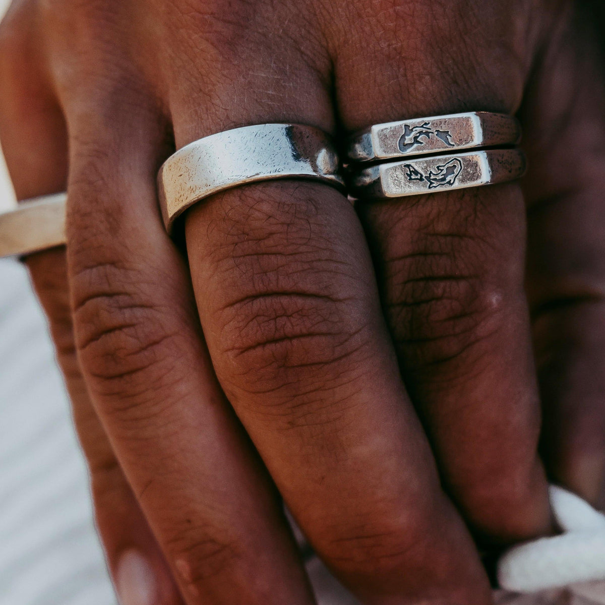 A close-up shot of a man's hand wearing two Billie Jo KOI I Rings stacked together, showing the detailed koi fish engraving and textured silver band.