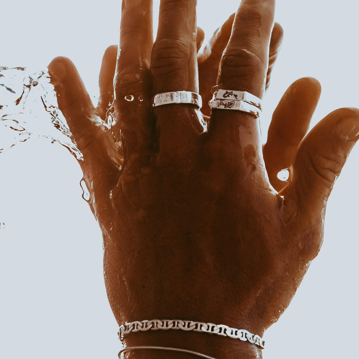 A dramatic shot of a man's hand, adorned with the Serenity Ring and other Billie Jo silver jewellery, under running water.