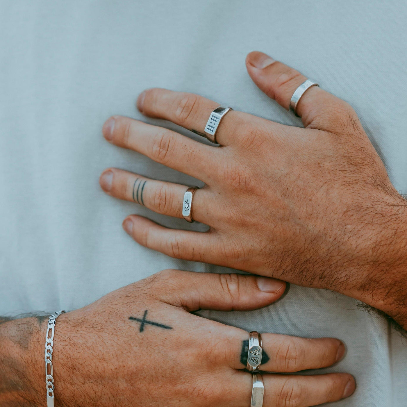 A lifestyle shot of a model's hands with tattoos, wearing multiple Billie Jo rings, including the ROSA I RING, against a neutral background.