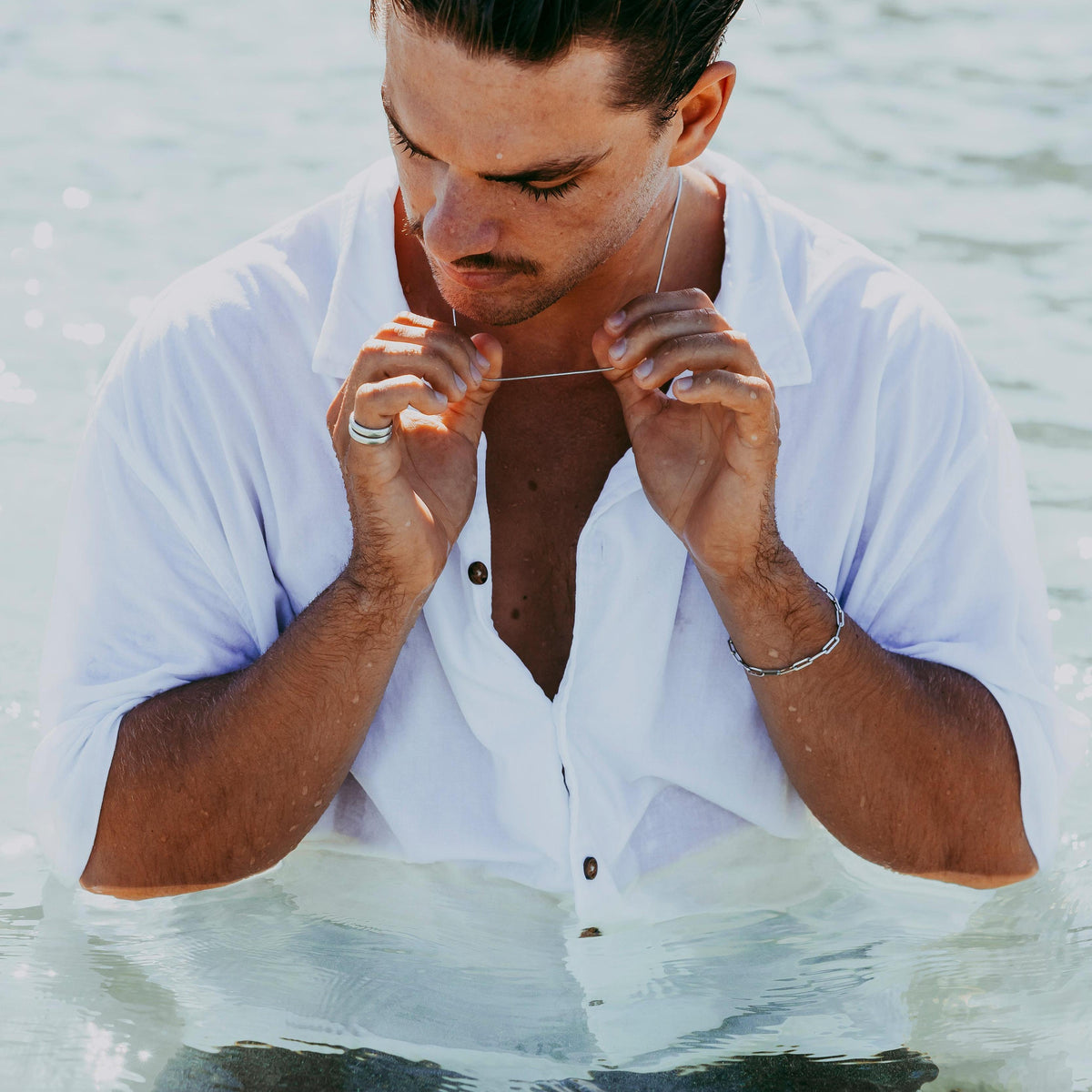 A man in a white shirt stands in the water, wearing the sterling silver Link Bracelet from Australian jewellery brand Billie Jo. A modern, masculine lifestyle shot.