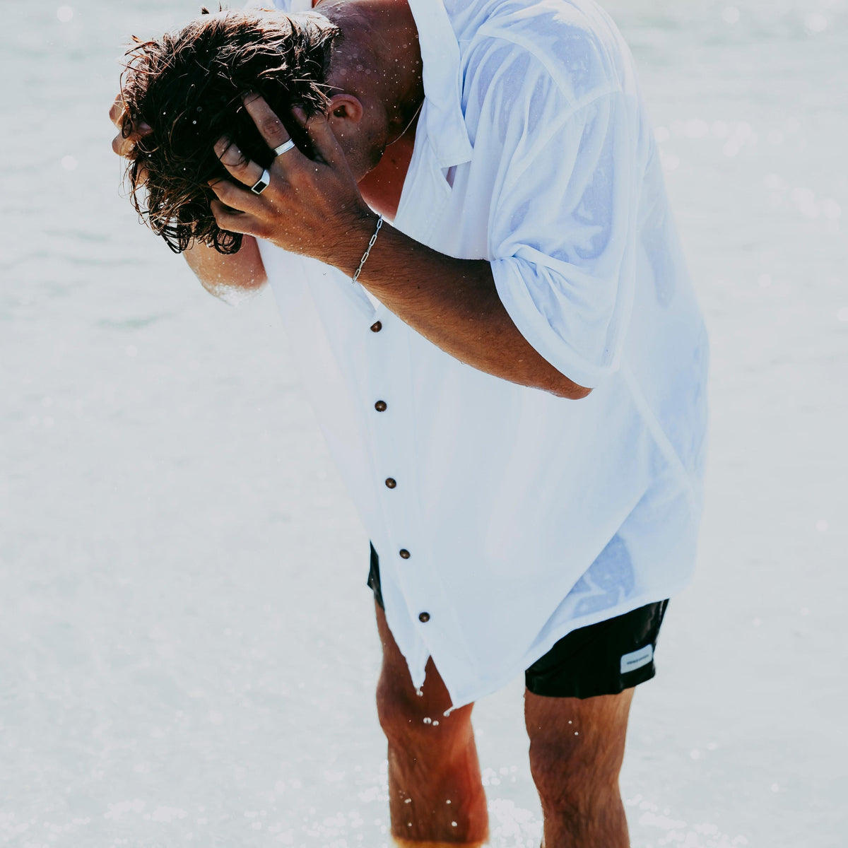 A man at the beach with wet hair, wearing a white shirt and the sterling silver Link Bracelet from Billie Jo. A modern, masculine summer editorial shot.