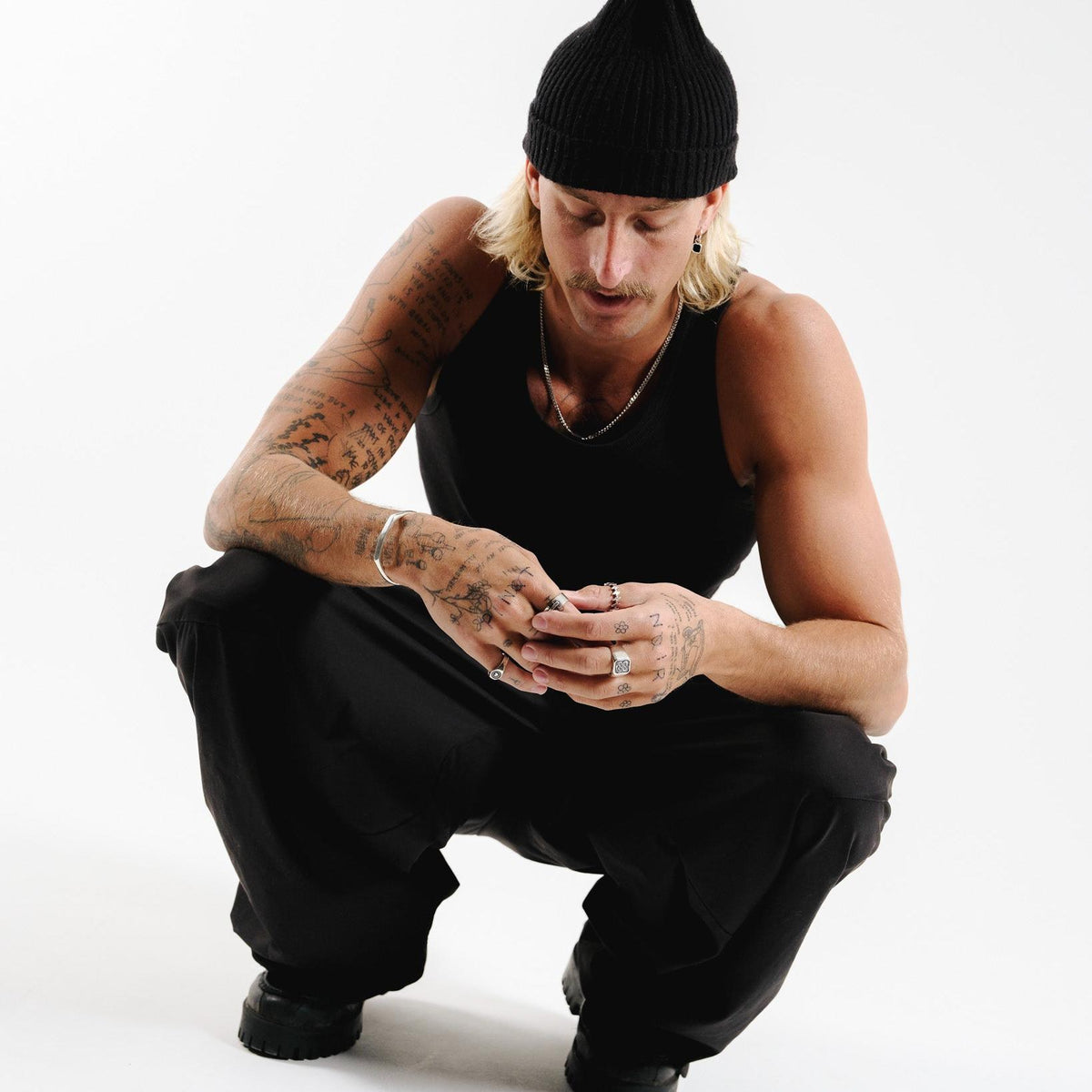 A model wearing the Billie Jo Surge Ring, crouched in a studio setting. The sterling silver ring is part of a modern, masculine look.
