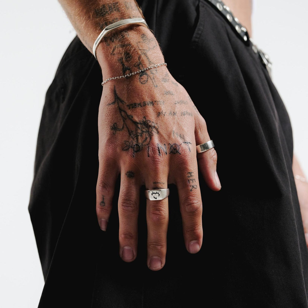The sterling silver Ember Ring from Billie Jo, styled on a man's tattooed hand with other silver jewellery against a black outfit.