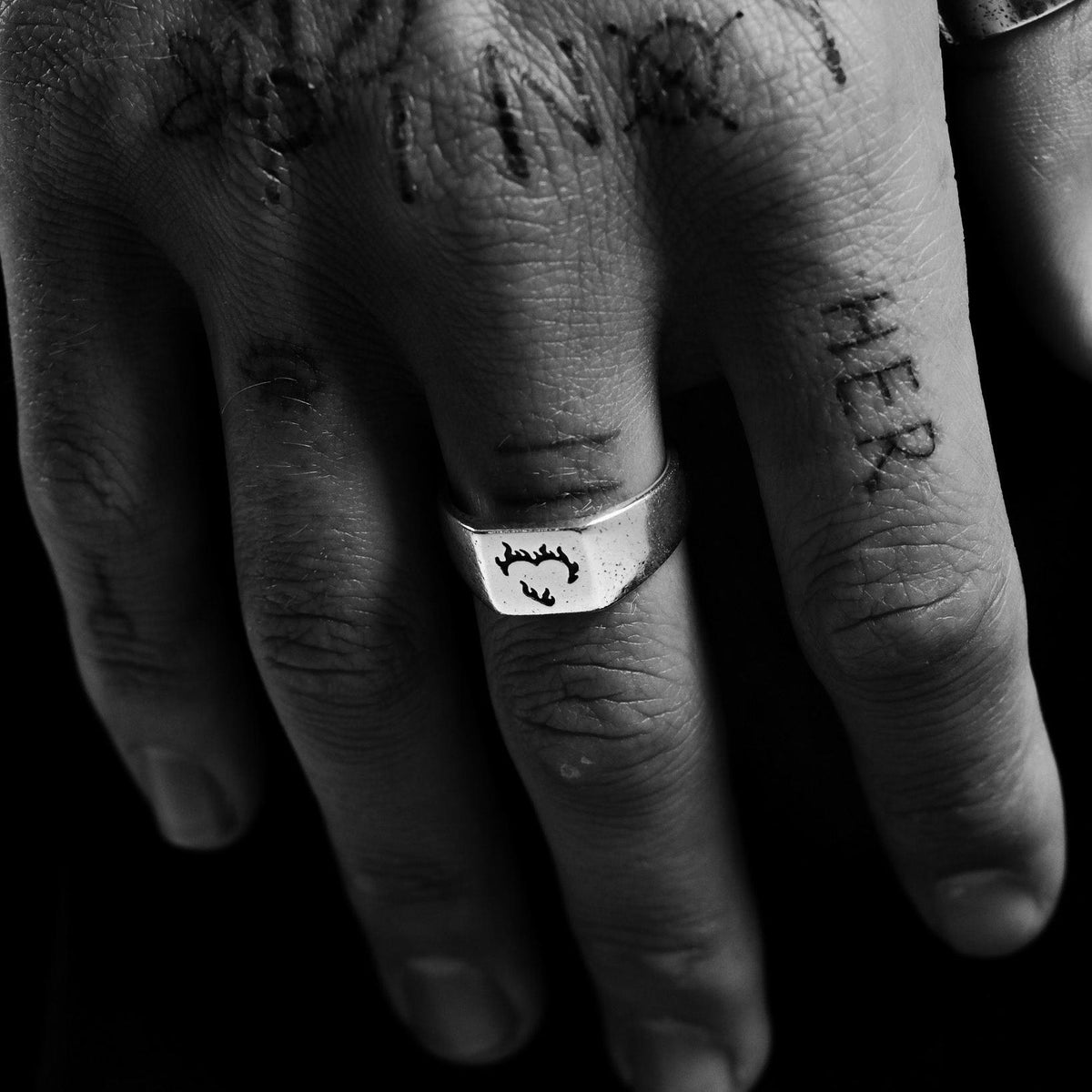 A close-up of the Ember Ring by Billie Jo, worn on a tattooed hand. The sterling silver ring features a unique flaming heart design.