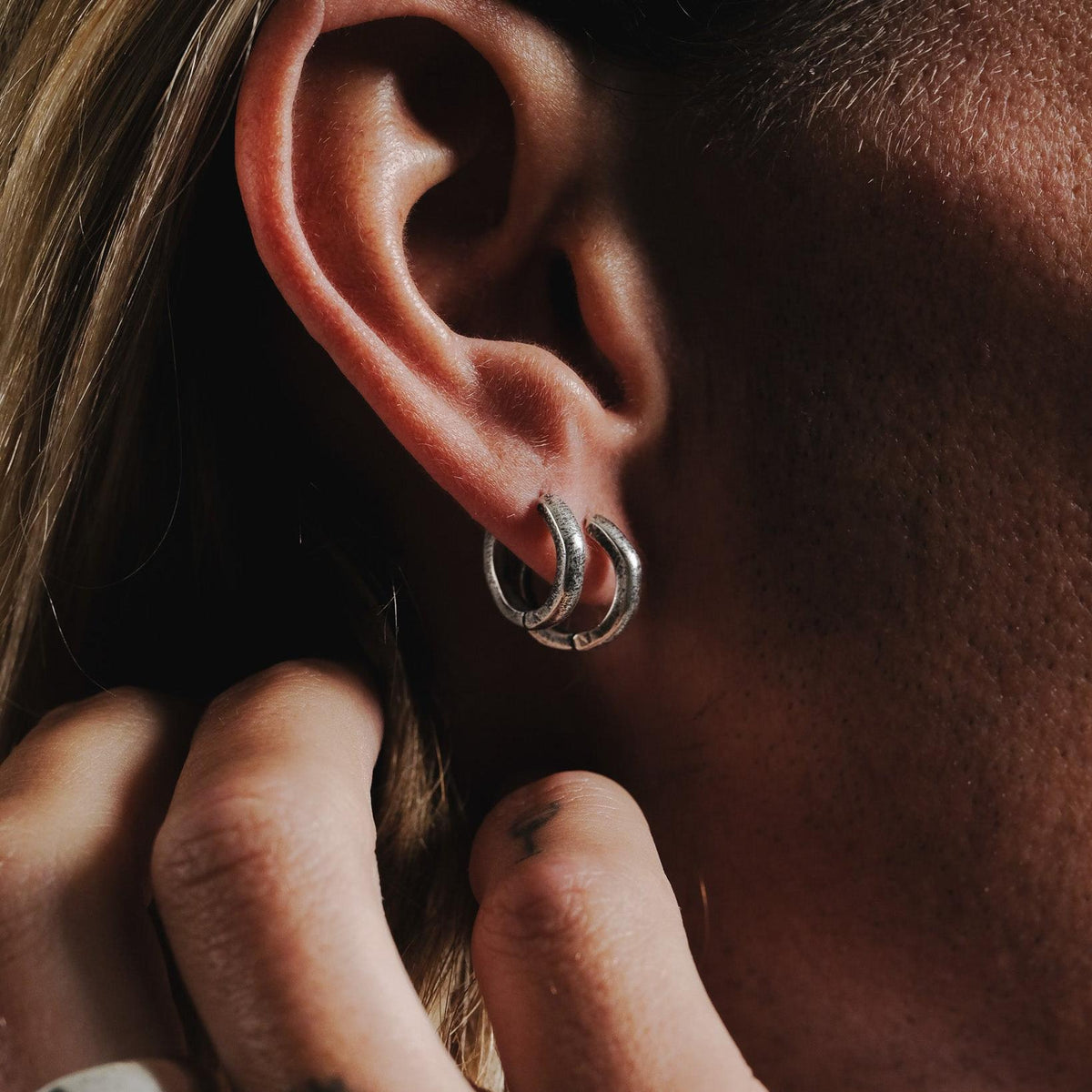 Close-up of a man wearing two sterling silver Billie Jo Lumina hoop earrings in a stacked, modern style