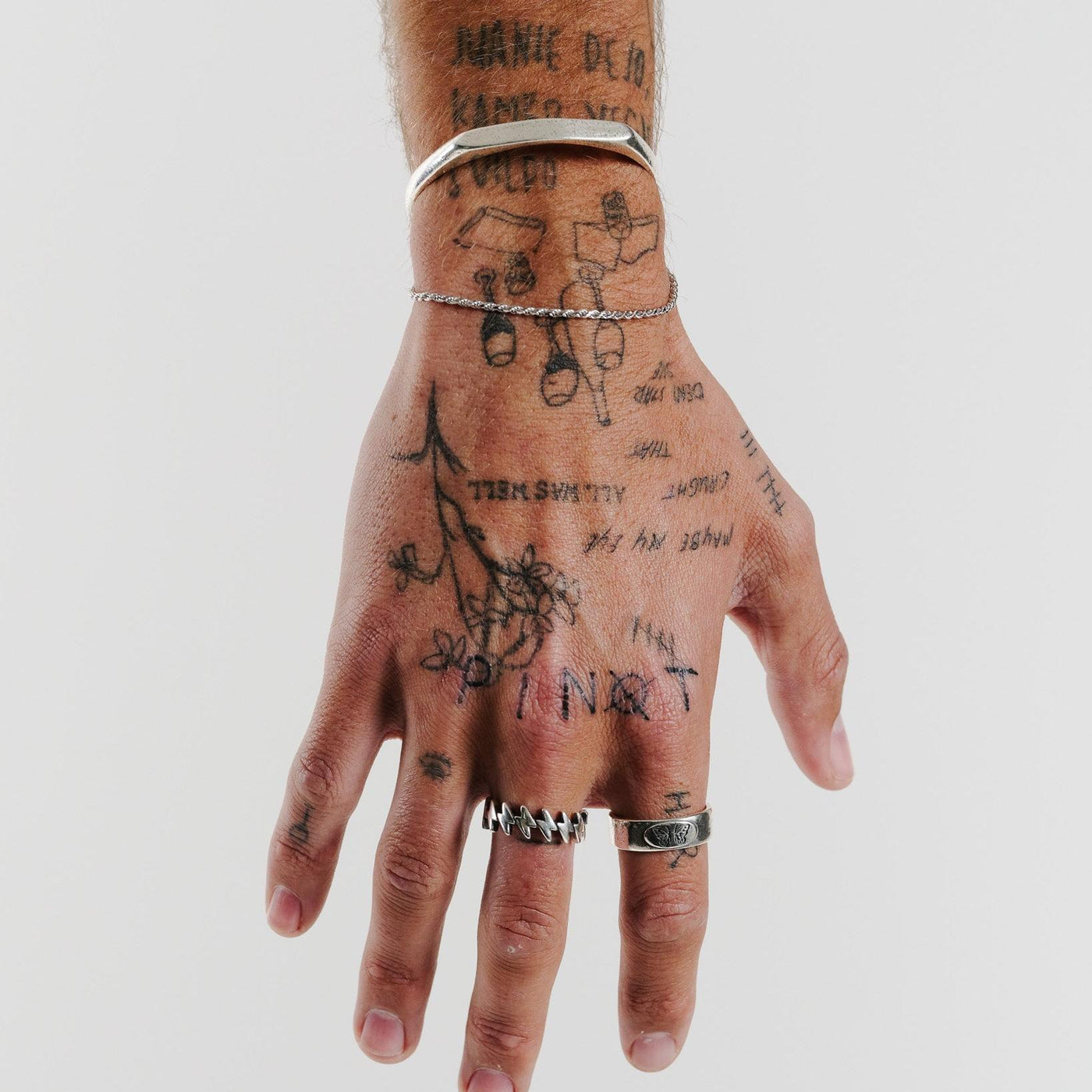 A hand with multiple tattoos wearing the sterling silver Surge Ring from Billie Jo, showcasing its bold and edgy design.