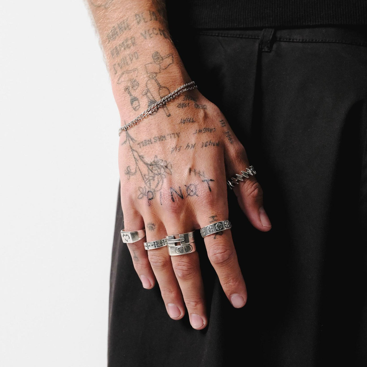 A tattooed hand wearing a stack of silver rings, including the Ember Ring by Billie Jo, showcasing a modern, layered men's jewellery look.