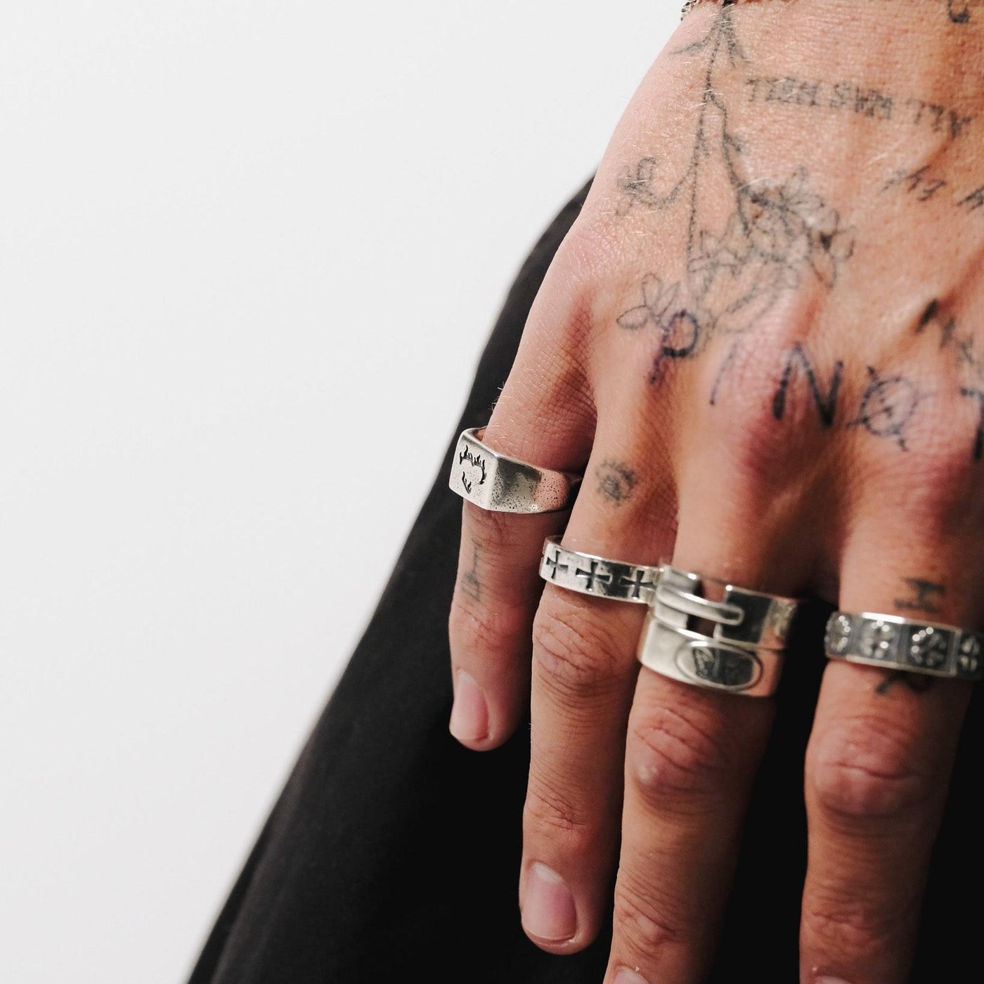 A side view of a man's tattooed hand, wearing the Ember Ring and other silver rings from Billie Jo, creating a bold, masculine aesthetic.