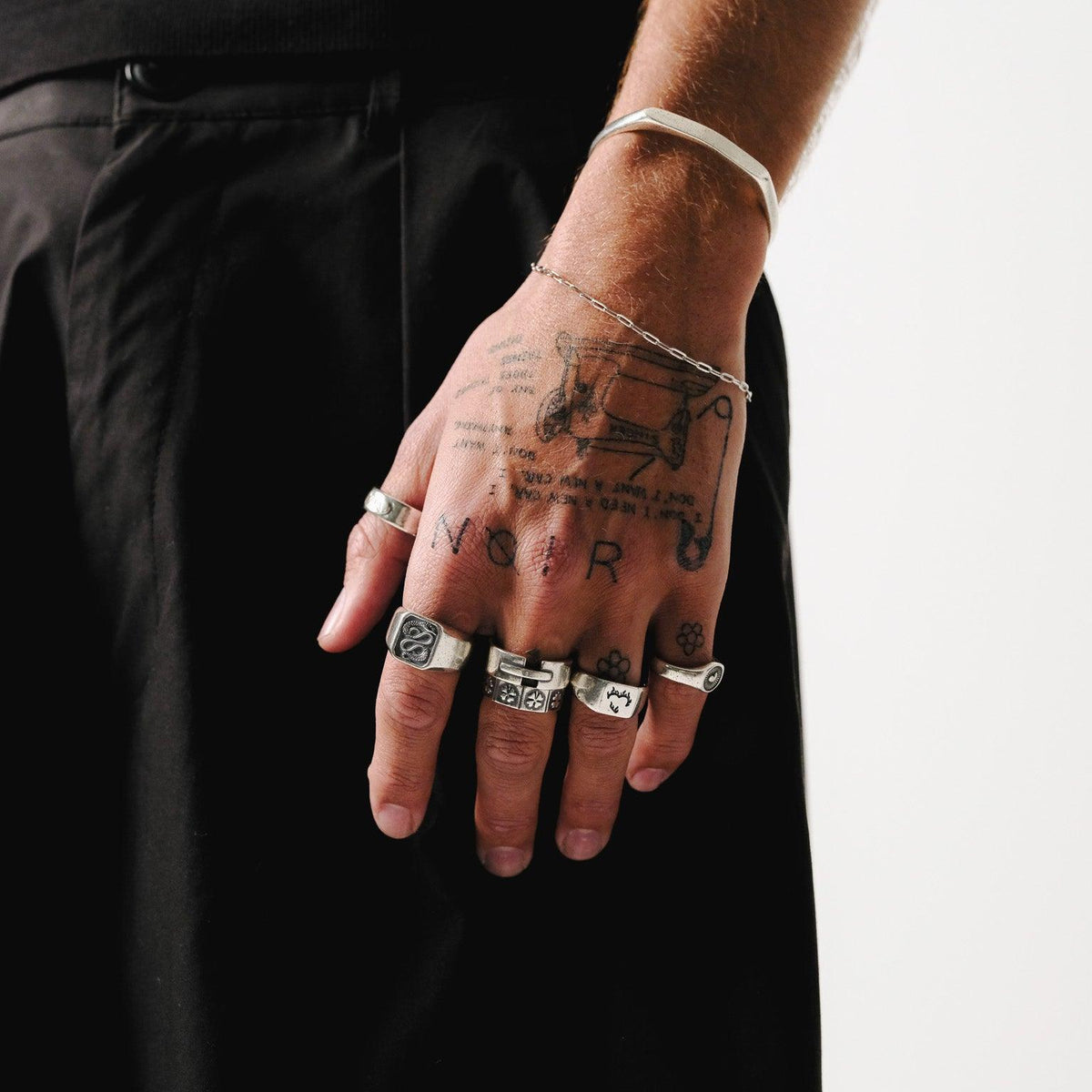 A collection of men's sterling silver rings from Billie Jo, including the Ember Ring, styled on a tattooed hand for an edgy, modern look.