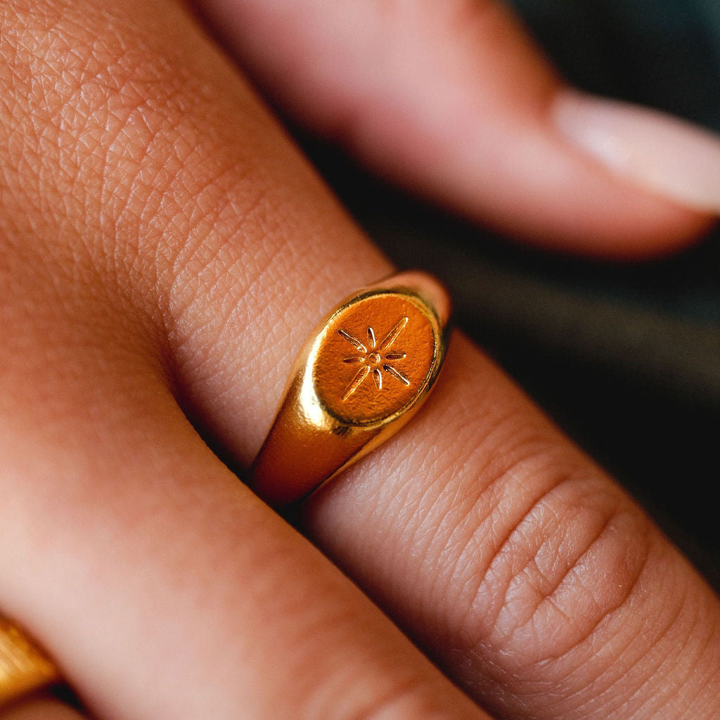 A detailed close-up of the Billie Jo Luminous Ring in gold, showing the texture of the 18k gold vermeil and the crisp starburst engraving on the signet.