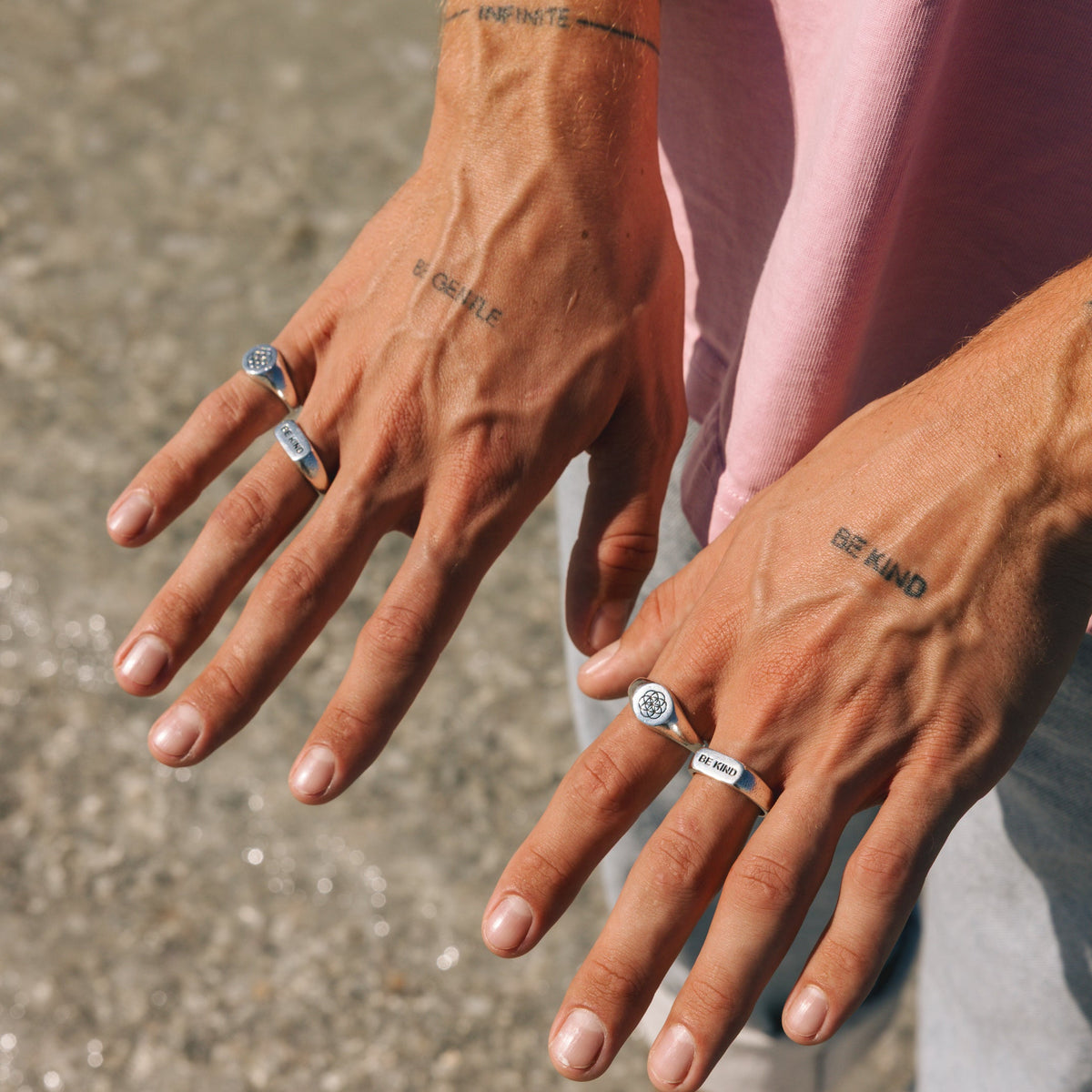 A detailed shot of a man's tattooed hands wearing a stack of sterling silver rings, including the iconic UNITY RING from Australian brand Billie Jo.