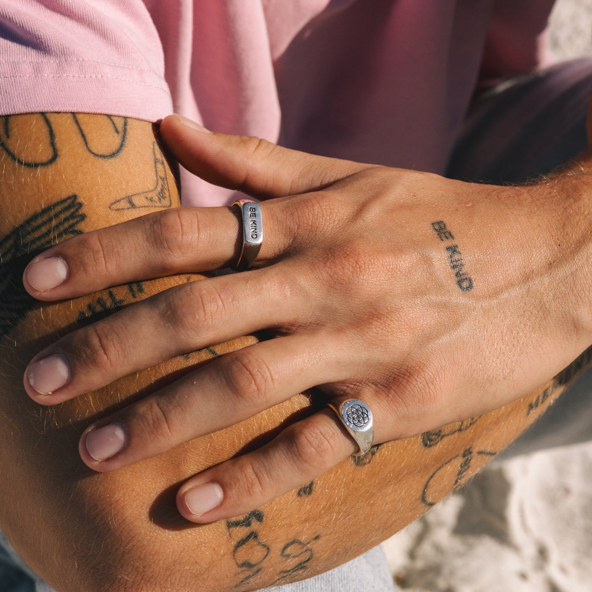 On-hand shot of the BE KIND ring from Billie Jo, worn by a man with tattoos on a sunny day, showcasing its casual and stylish vibe.