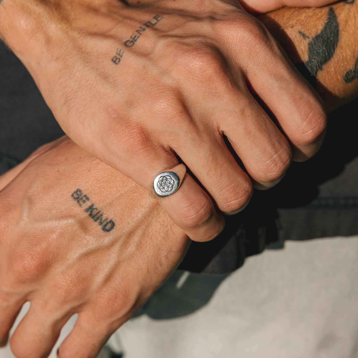 A close-up on-hand shot of the sterling silver UNITY RING by Billie Jo, styled on a tattooed hand with 'BE GENTLE' and 'BE KIND' tattoos.