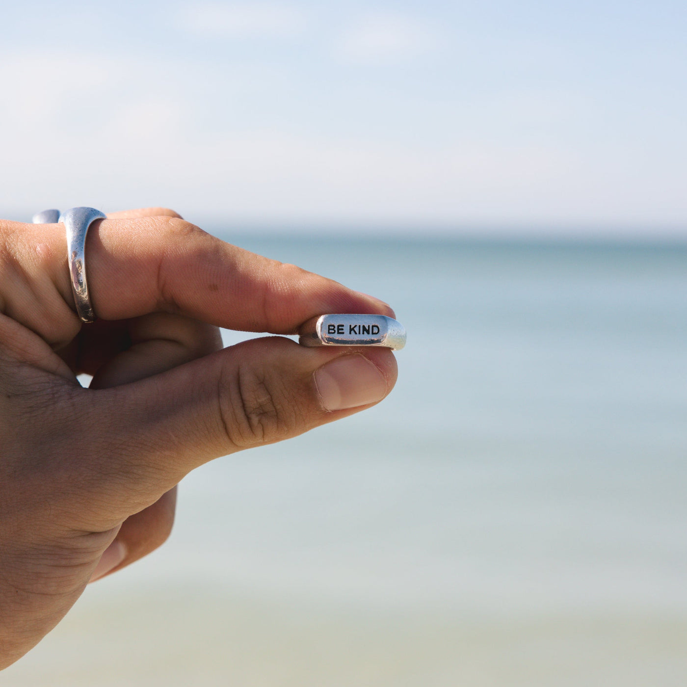 Close-up of the Billie Jo BE KIND ring held against a beach backdrop, highlighting the detailed engraving and polished 925 sterling silver finish.