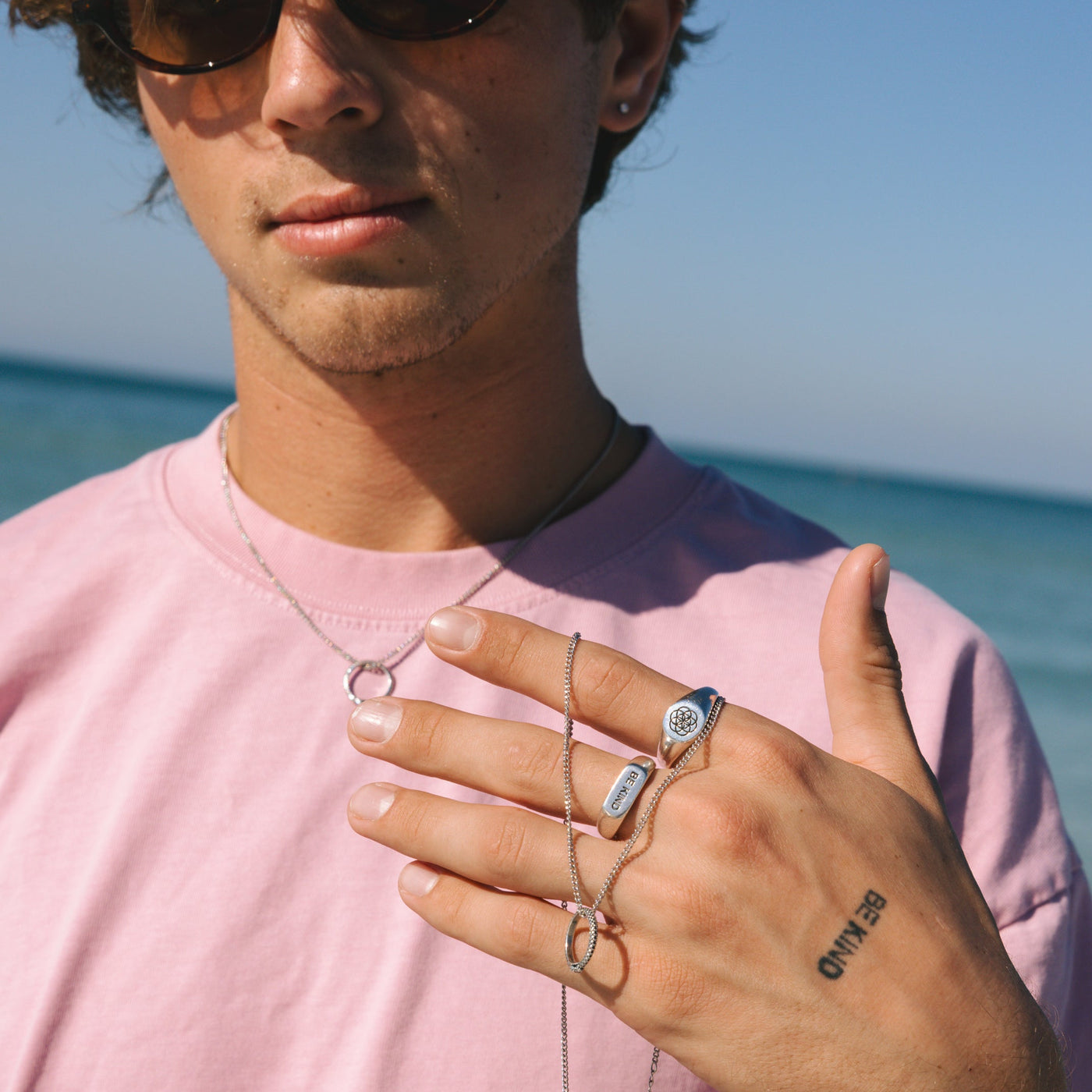 A man models the Billie Jo UNITY RING and layered silver necklaces on the beach, capturing the brand's relaxed Australian men's jewellery aesthetic.