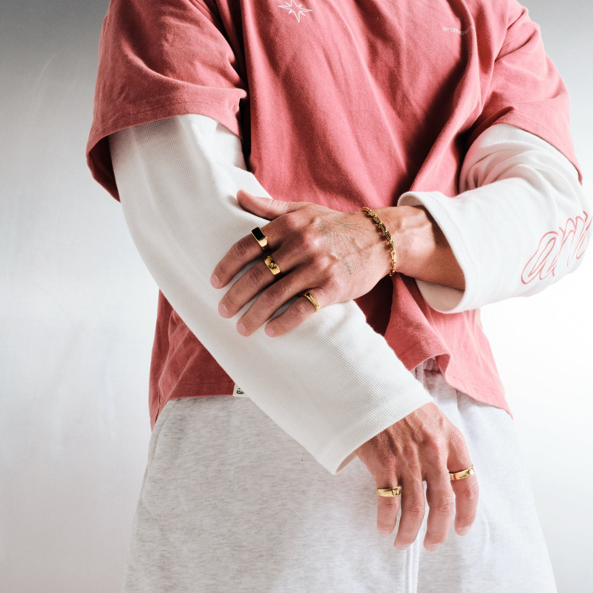 Man wearing gold stainless rings, arms folded across his body, with a gold chain bracelet