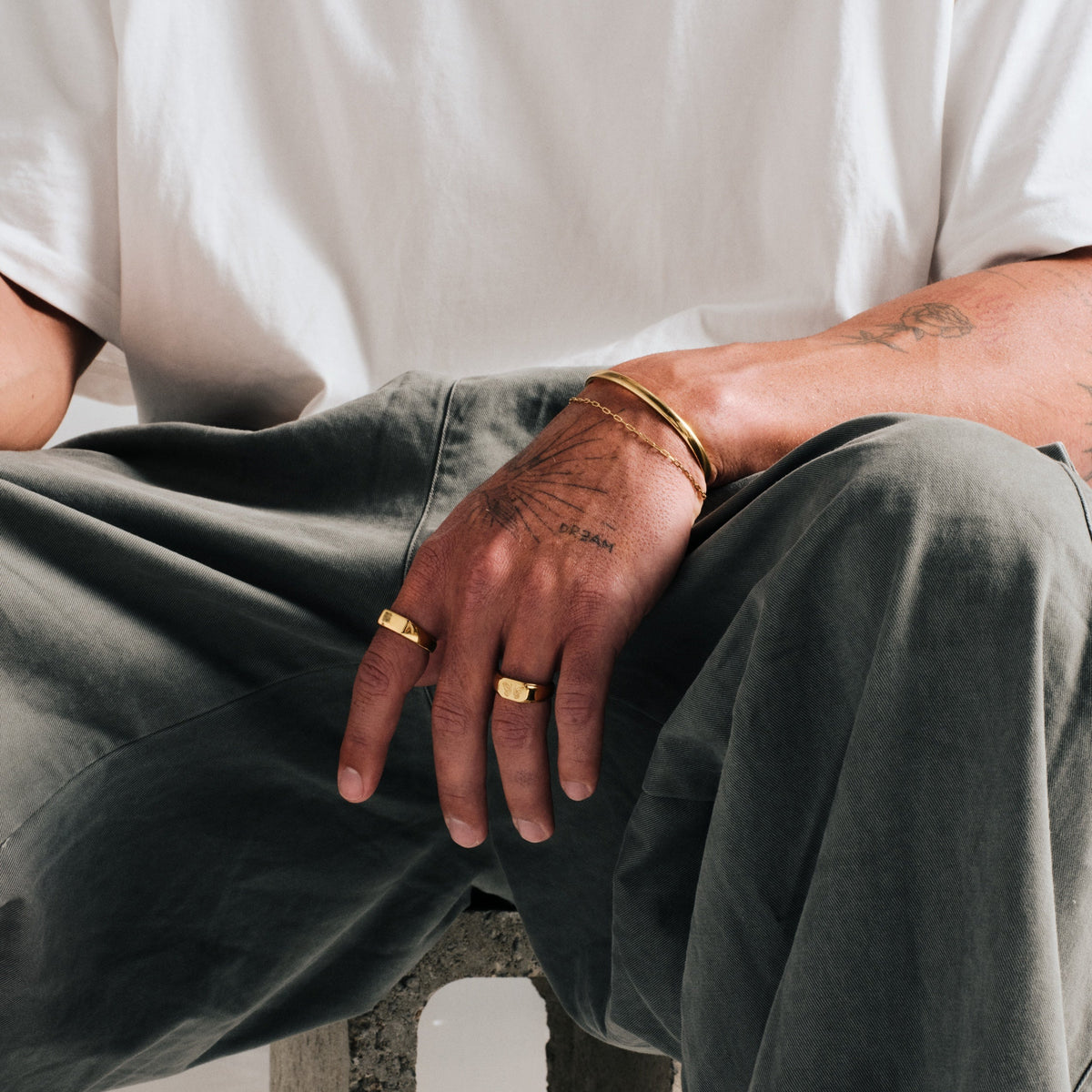 Men's Gold Drifter Cuff in 18k gold infused stainless steel, worn on his left wrist, seated, forearm resting on his knee