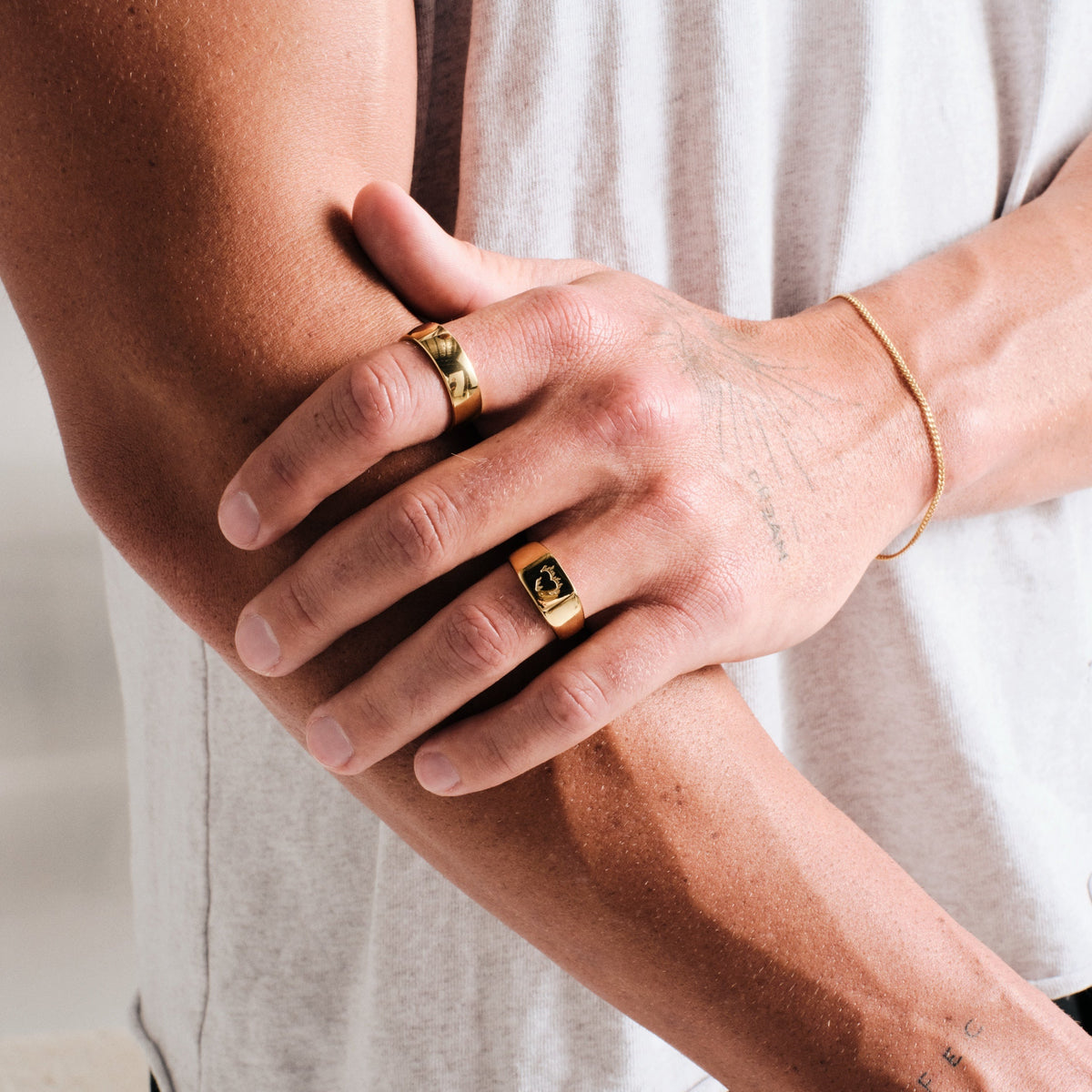 Men's Gold Ember Ring in 18k gold infused stainless steel, worn on his left ring finger, hand resting on his other forearm