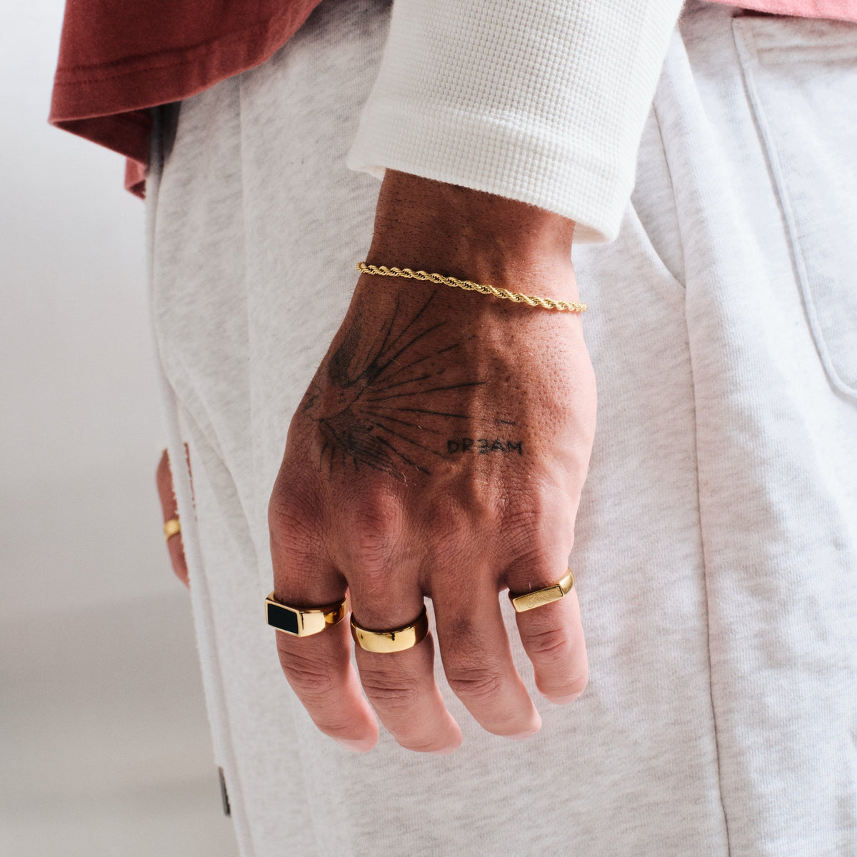 Men's Gold Koi II Ring in 18k gold infused stainless steel, in a stack, hand by his side, with a gold rope bracelet