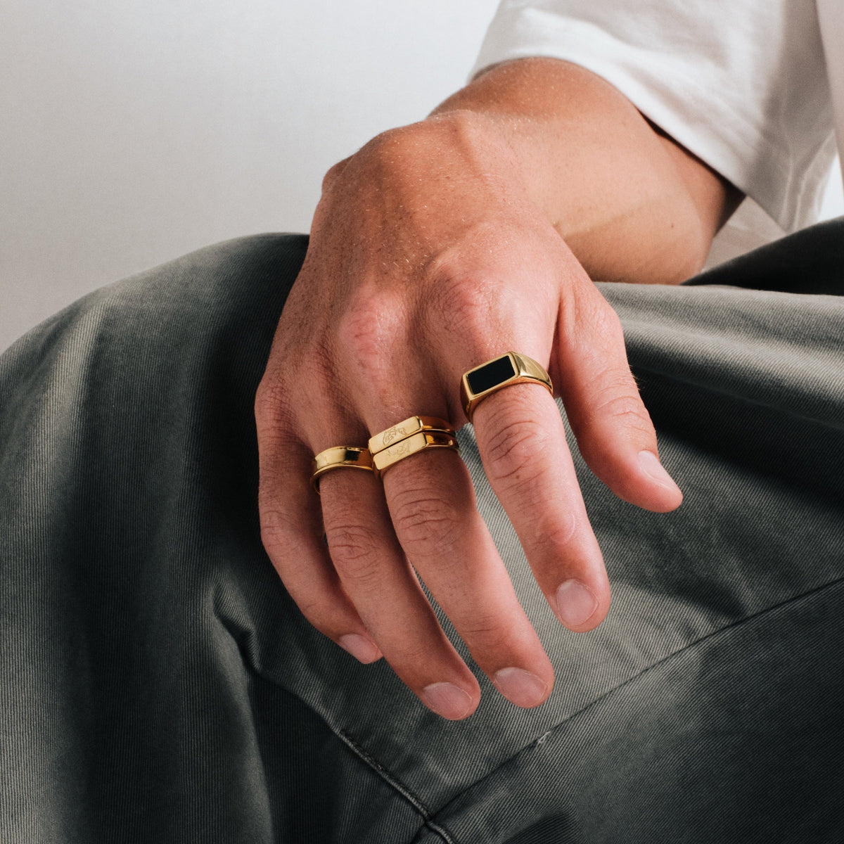 Men's Gold Koi Stackers in 18k gold infused stainless steel, both worn on the middle finger, hand resting on his knee