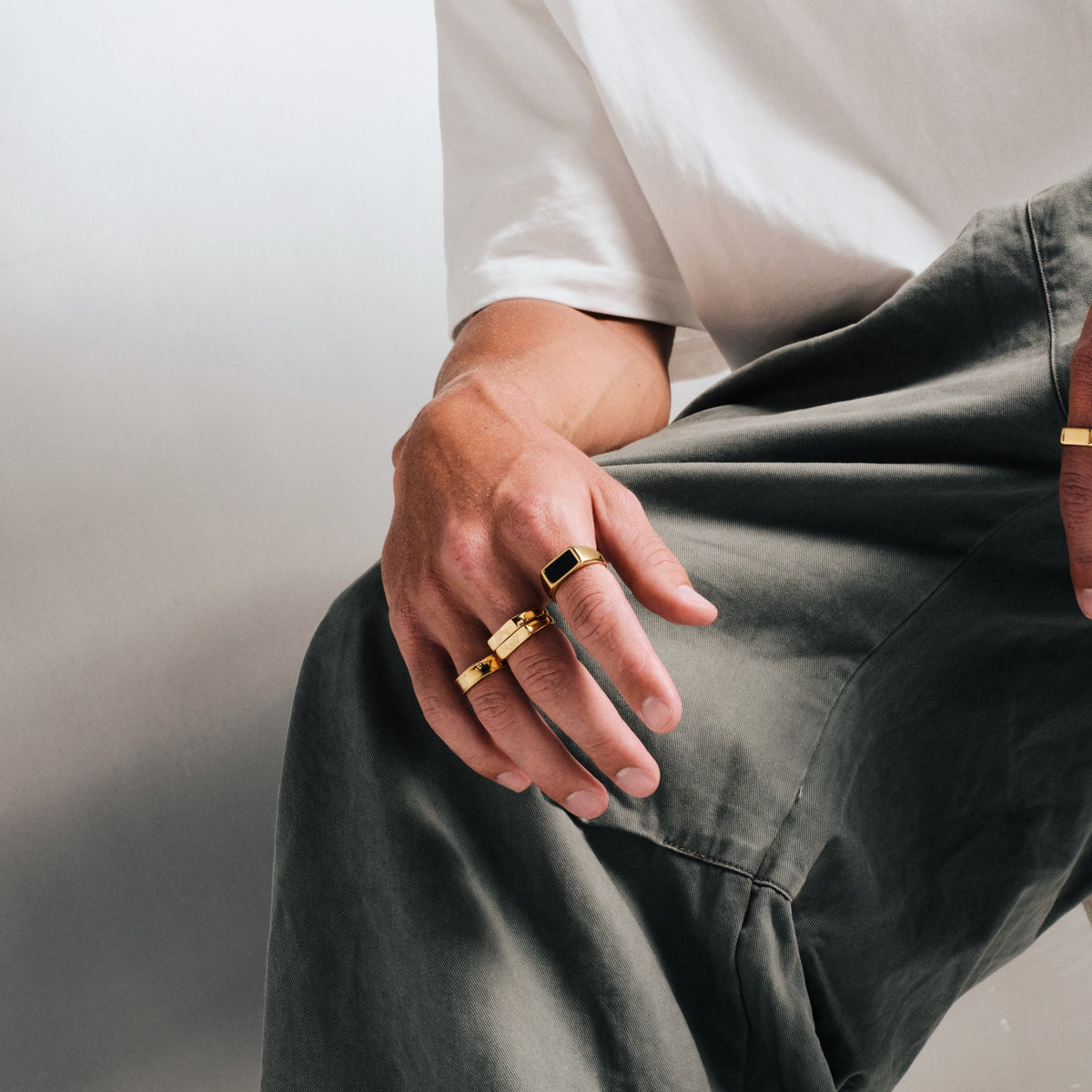 Men's Gold Koi Stackers in 18k gold infused stainless steel, both worn on the middle finger, hand resting on his knee
