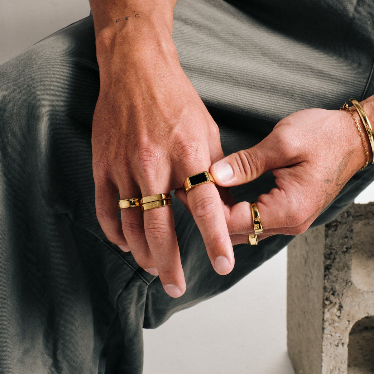 Men's Gold Koi Stackers in 18k gold infused stainless steel, both worn on his right middle finger, olive pants