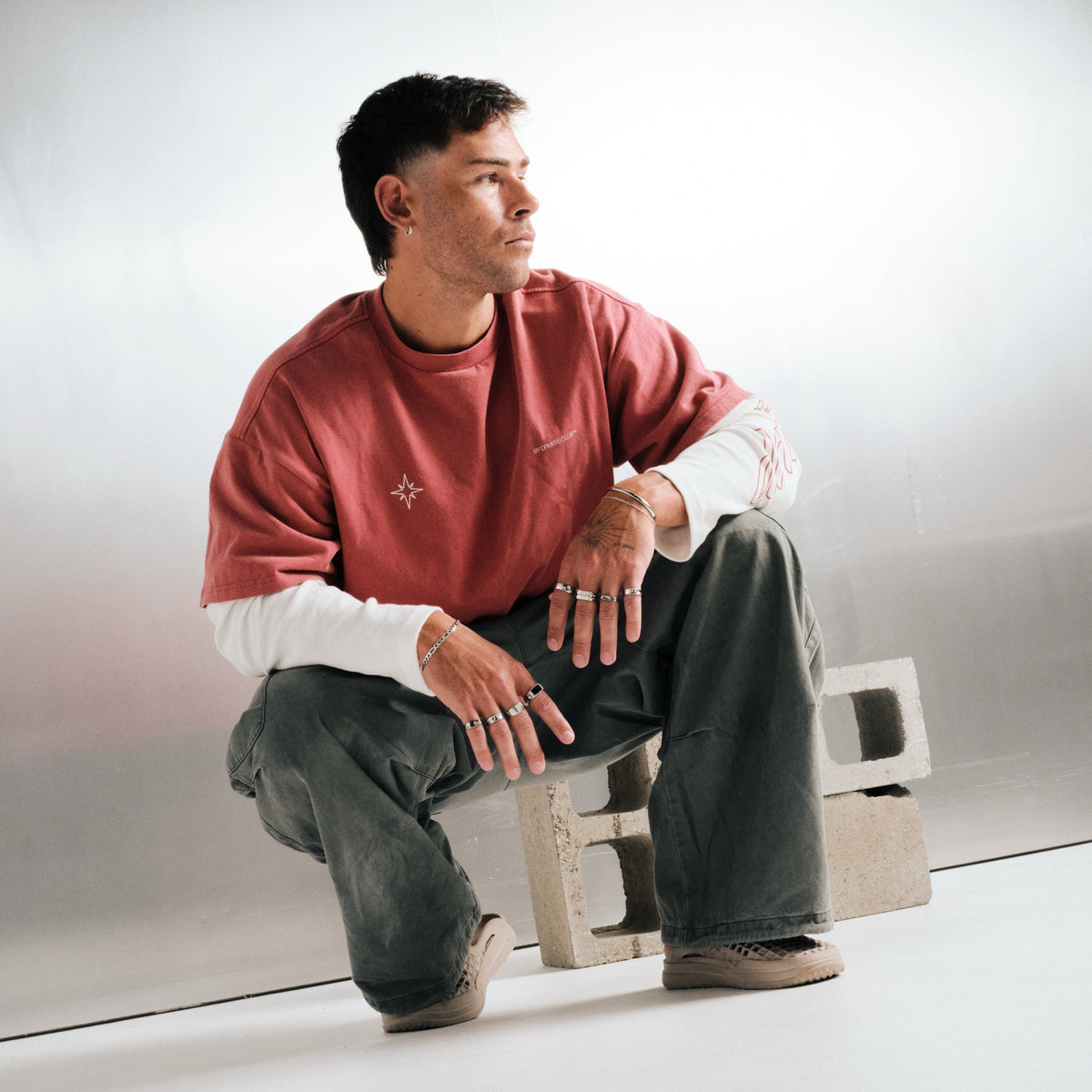 Man wearing silver finish stainless rings, crouched on a concrete block, with a steel chain bracelet, steel bangles