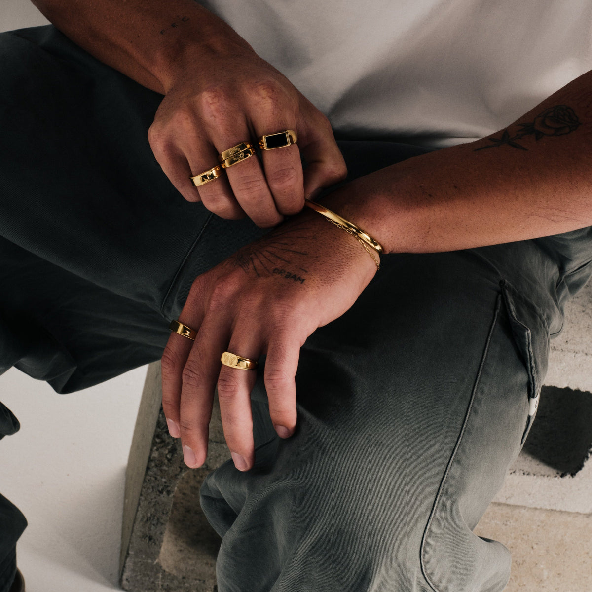 Men's Gold Revival Ring in 18k gold infused stainless steel, worn on the middle finger, white tee, olive pants