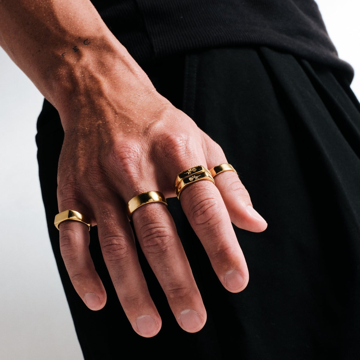 Man wearing gold stainless rings, hand hanging by his side, black tee, black pants
