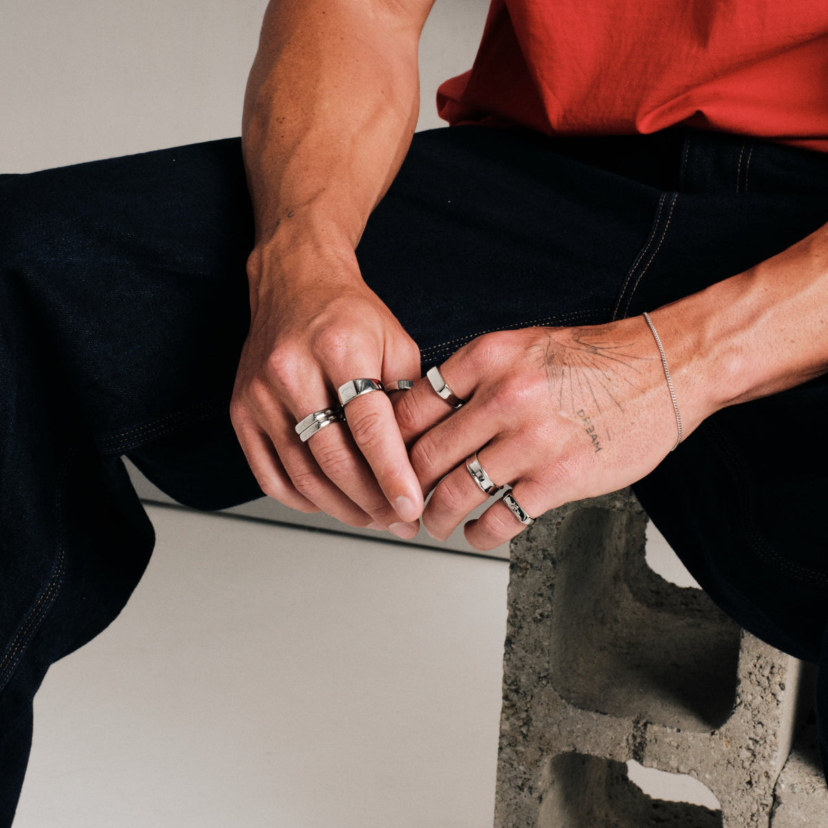 Men's Rosa Stackers in 316L stainless steel, silver finish, in a stack, seated on a concrete block, hands clasped on knee