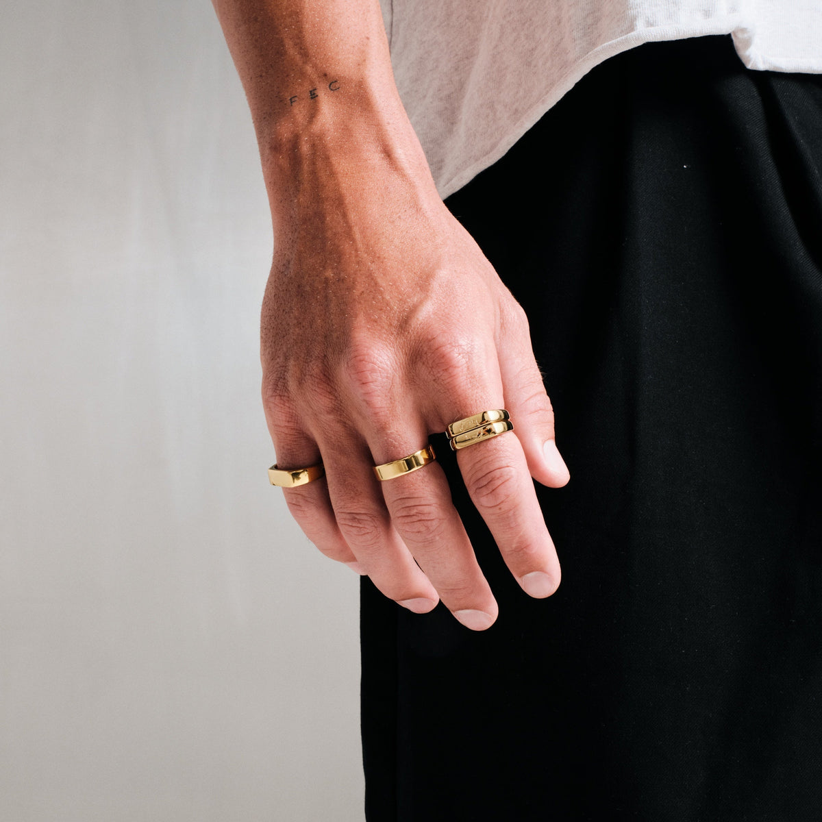 Man wearing gold stainless rings, hand hanging by his side, grey tee, black pants
