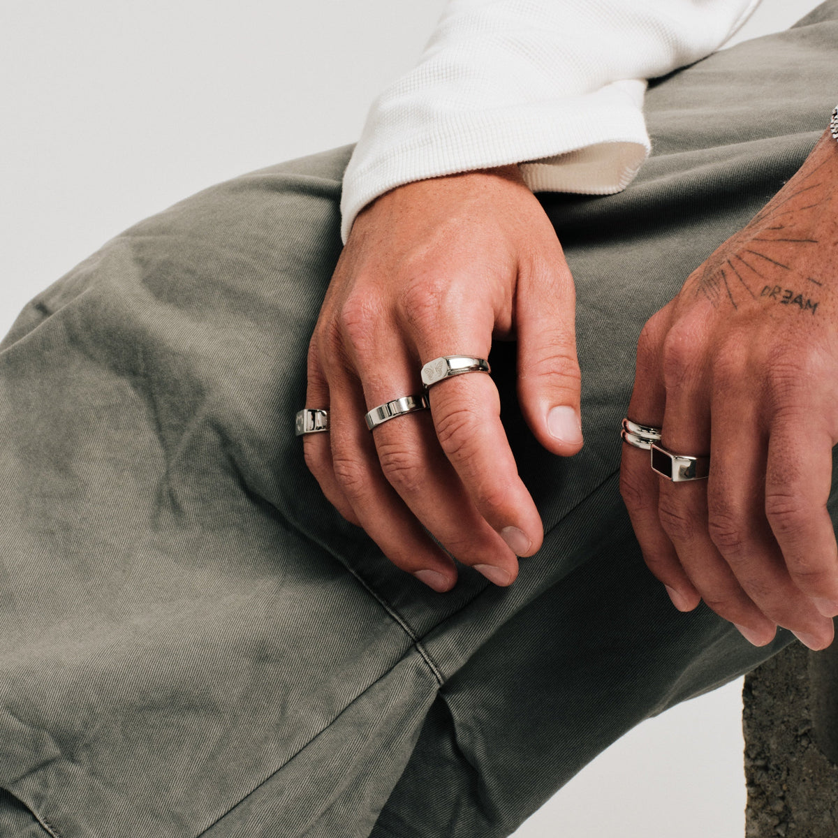 Men's Serenity Ring in 316L stainless steel, silver finish, worn on the middle finger, seated, hands resting over his knee