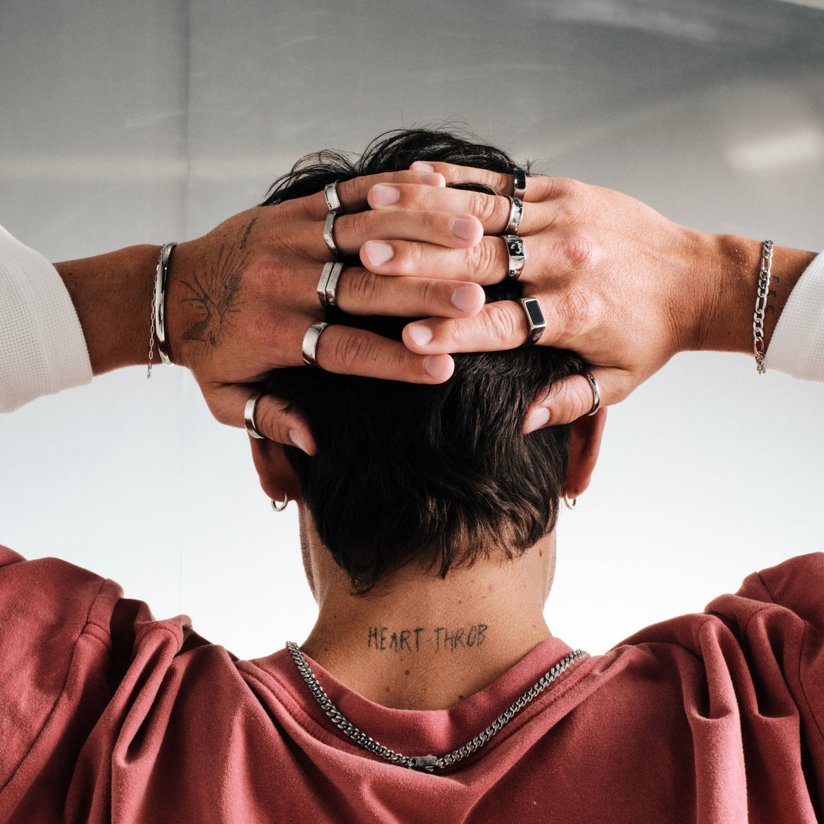 Man wearing silver finish stainless rings, hands behind his head, seen from behind, red tee