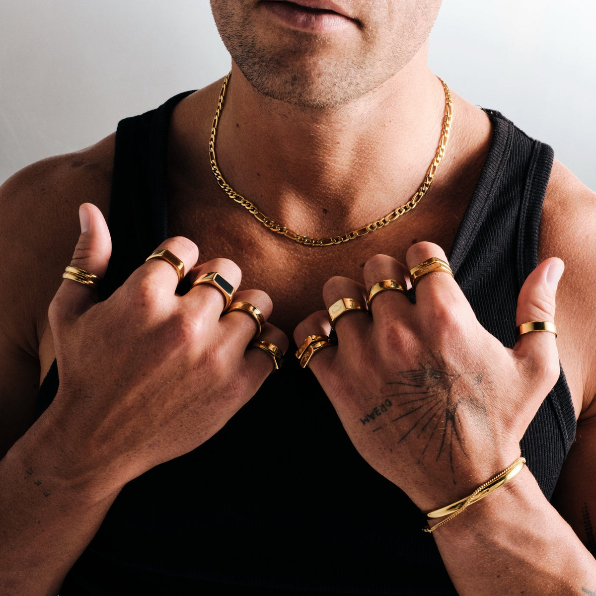 Men's Gold Stacker Rings in 18k gold infused stainless steel, both worn on the thumb, hands on his chest, black singlet