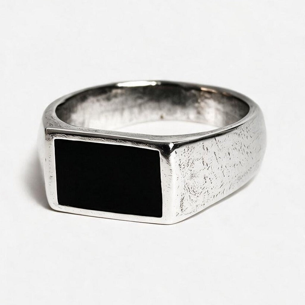 A silver signet ring with a textured band and a rectangular black inlay, photographed on a clean white background.