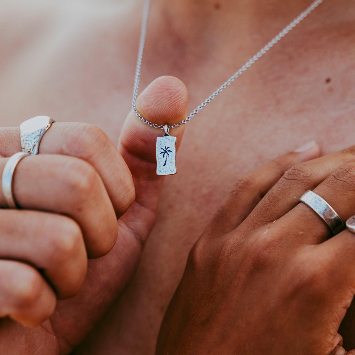 A close-up shot of the sterling silver Paradiso Pendant from Billie Jo, held between two fingers to showcase the detailed palm tree engraving.