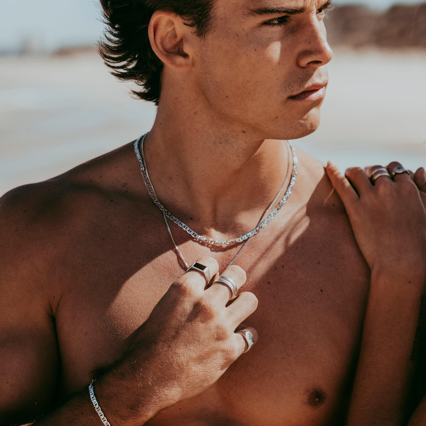 A man on a beach, wearing the Billie Jo Onyx Ring and other silver jewellery, with a woman's hand on his shoulder.