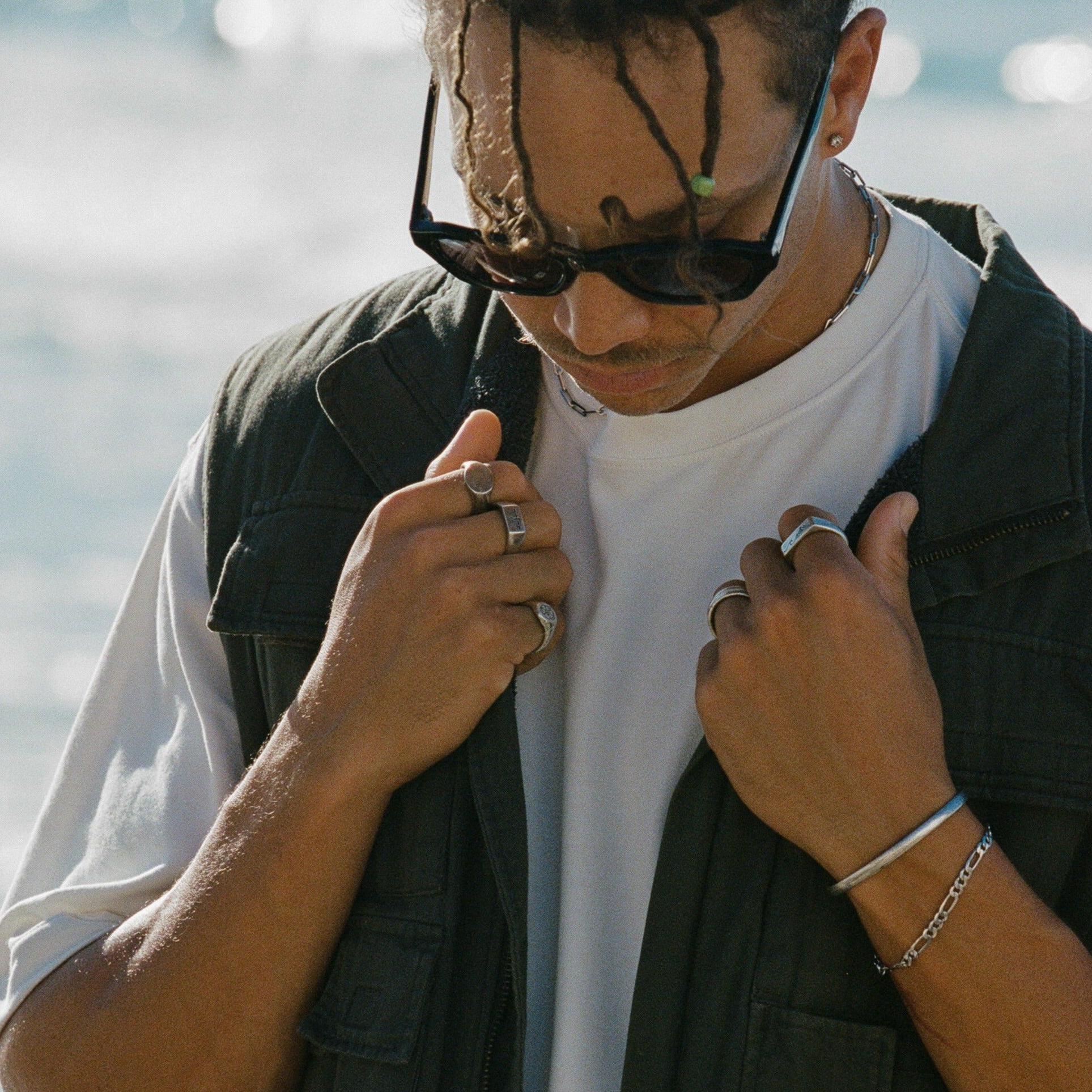 A male model wears the sterling silver Figaro Bracelet from Billie Jo, styled with a cuff and multiple rings. This on-hand shot shows how the bracelet can be layered for a modern, masculine look.